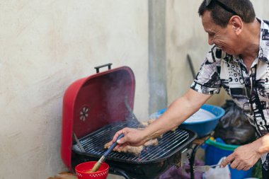 Adam arka bahçede ailesinin öğle yemeği için barbekü ızgarasında et hazırlıyor..