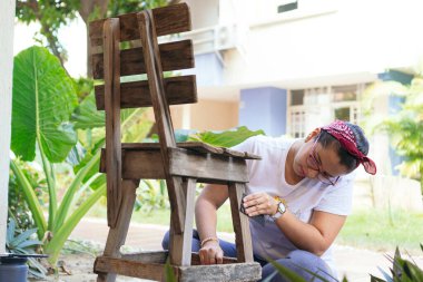 Genç bir kadın, evinde eski bir ahşap sandalyeyi yeniler ve geliştirir.