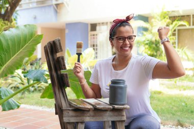 Arka bahçedeki İspanyol kadın eski bir sandalye boyuyor ve gülümsüyor.