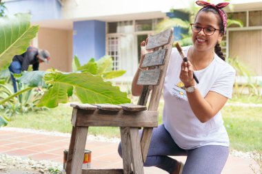 Genç kadın arka bahçede eski bir sandalye boyuyor.