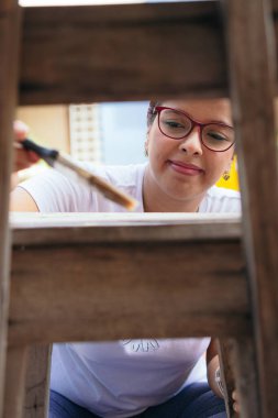 Latin bir kadın eski bir sandalyeyi boyuyor ve evde eğleniyor..