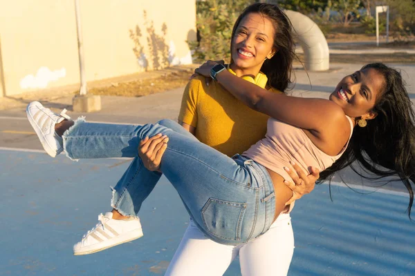 Two young women laugh, one carrying the other.