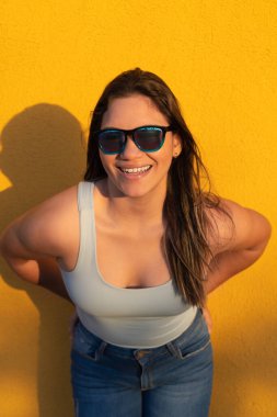 Sarı arka planda gülümseyen güneş gözlüklü kadın. Kopya alanı olan güzel bir kadın model.