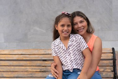 Anne ve kızı kameraya sarılıp gülümsüyor..