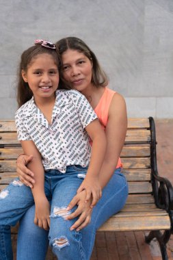Latin anne ve kızı kameraya sarılıp gülümsüyor..