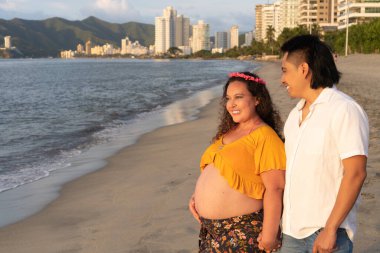 Genç hamile bir çift sahilde yürüyor.