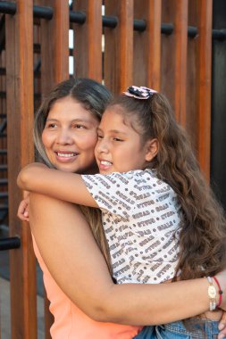 İspanyol anne parkta kızına sarılırken gülümsüyor.