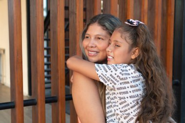 Anne parkta kızını kucaklarken gülümsüyor.