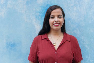 Kırmızı gömlekli kadın mavi duvarın önünde duruyor.