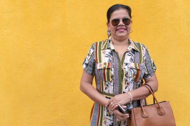 Sarı duvarın önünde gülen olgun bir kadın.