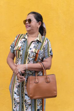 Sarı duvarın önünde düşünceli bir kadın duruyor.