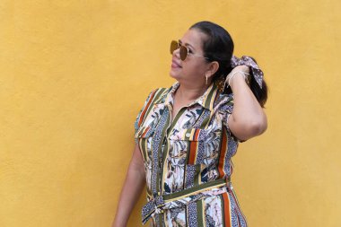 Sarı arka planda poz veren olgun bir kadın elbise giyiyor.