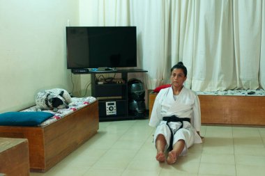 Evde siyah kuşaklı beyaz kimonolu bir kız var.