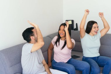 Arkadaşlar galibiyet golünü atarken beşlik çakıyor. Futbol hayranları kanepede otururken içki ve atıştırmalıkların tadını çıkarıyorlar. Evde çok eğleniyorlar..