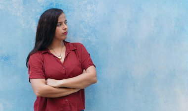 20 yaşında genç bir Latin. Kolları mavi duvarda çapraz duruyor..