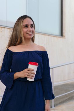 Sokakta kahveyle gülümseyen sarışın iş kadını portresi.