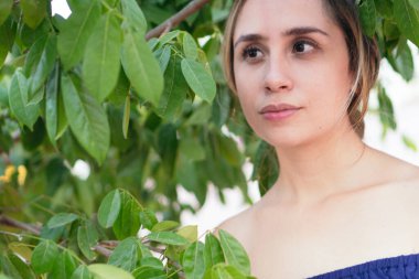 Latin kadın yemyeşil bir parkta çeşitli bitkilerle çevriliyken poz veriyor.