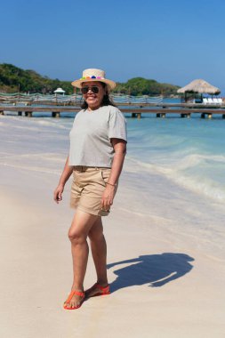 Şapkalı kadın sahilde eğleniyor.