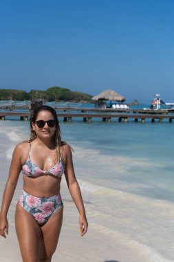 Genç bir kadın güneşli sahilde yürüyor.