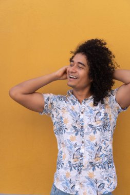 Afro saçlı hippi bir adam sokakta dikilip yüzünü kaçırırken saçlarına dokunuyor.