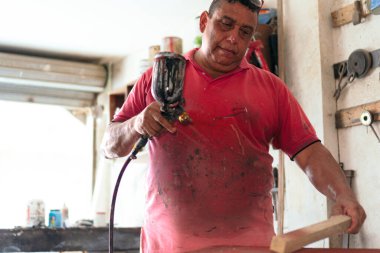 Marangoz atölyesinde bir sandalye boyuyor.