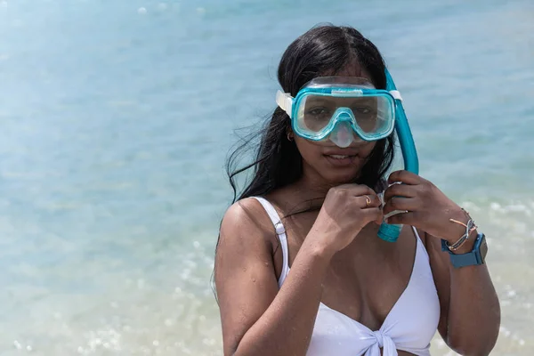 African woman with wet body and looking at camera while standing in the sea and adjusting protective goggles.