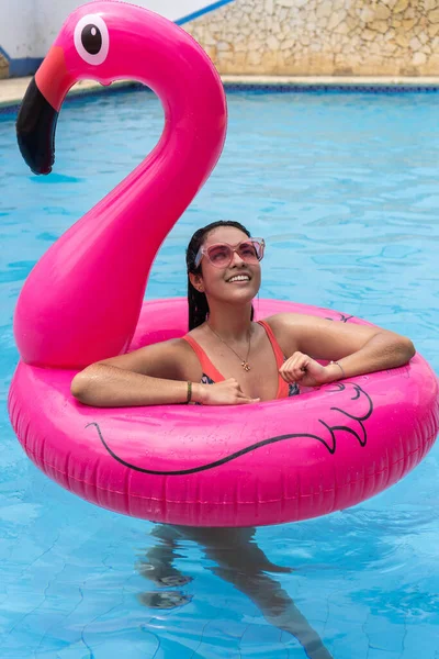 Latin Woman standing on an inflatable ring floating in the pool