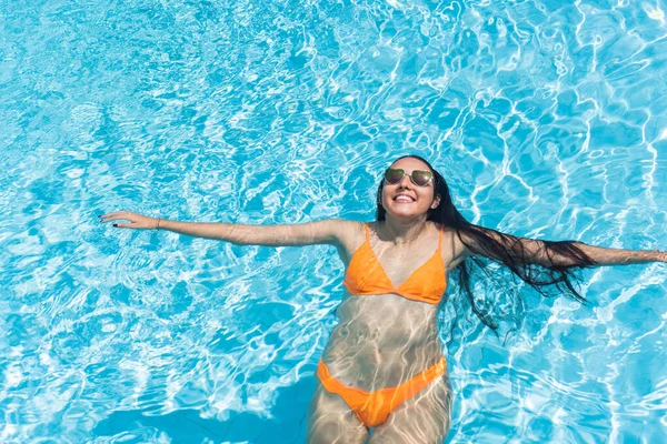 Serene woman in orange bikini floating in sunny summer swimming pool