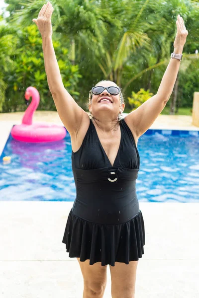 Older woman in the rain at a luxury swimming pool during summer vacations