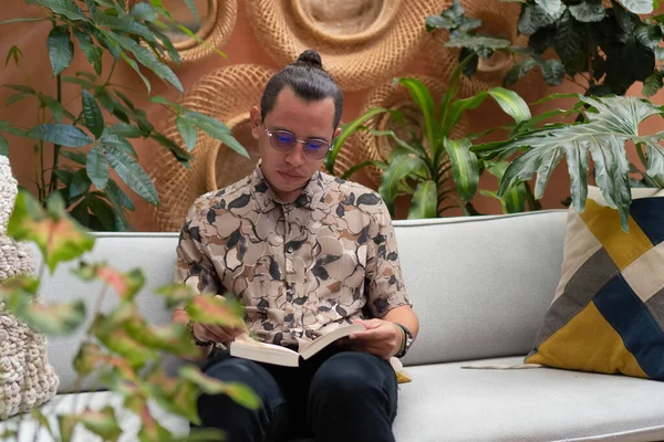 Koltukta oturup kitap okuyan bir adam. Genç adam rahat dairesinde kitap okuyor..