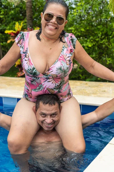 Older couple having fun in the pool in the sunlight.