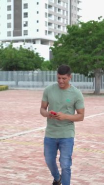 Young man with freckles walking and smiling while using her cell phone outdoors.