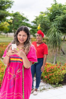 Latin woman using a cell phone and waiting for her friend clipart