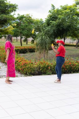 Latin woman performing a dance while her friend takes photos and videos with her cell phone in a city park. Creation of content for social networks.