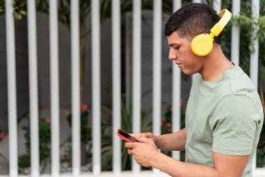 Young man using smartphone and listening to music with bluetooth headphones.