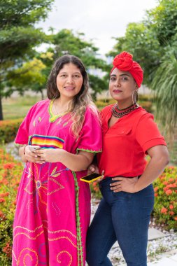 Two Latinas standing in the park, looking at the camera