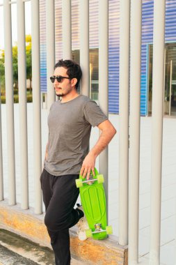 Hispanic man with sunglasses and skateboard in the park on a sunny day.