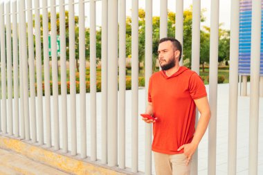 Bearded young man checking his cell phone in the park on a sunny day.
