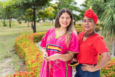 Two multi-ethnic women standing in the park, looking at the camera.