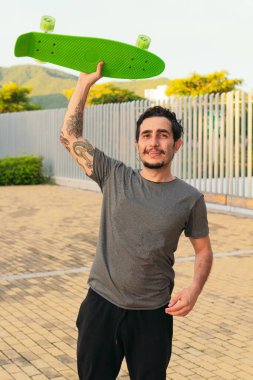 Parktayken elinde kaykayla dolaşan İspanyol bir adam.