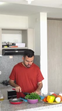 Latin bir adam evde mutfağında sağlıklı bir yemek hazırlarken kesim tahtasıyla sebze doğruyor.