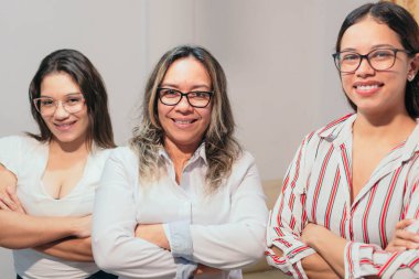 Bir grup iş kadını kollarını kavuşturup ofiste duruyorlar.