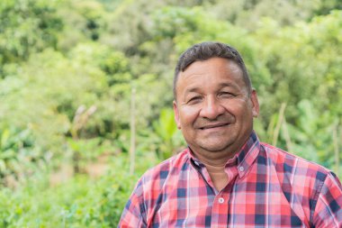Pozitif orta yaşlı bir adam sahada durup kameraya bakıp gülümsüyor.