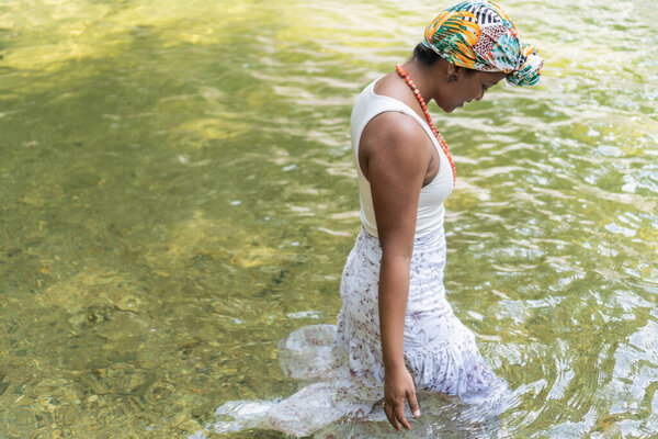 A black woman enters a river in the forest.
