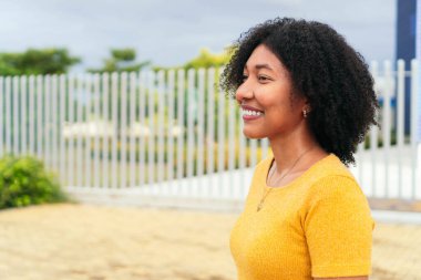 Parkta gülümseyen Afro bir kadın.