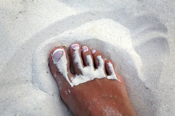 foot girl with white pedicure in the sand