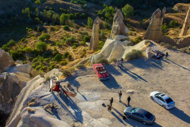Kapadokya, Nevsehir, Türkiye-Eylül-2021: Peri bacalarıyla fotoğraf çeken çiftler. Kırmızı vintage araba. Üst görünüm