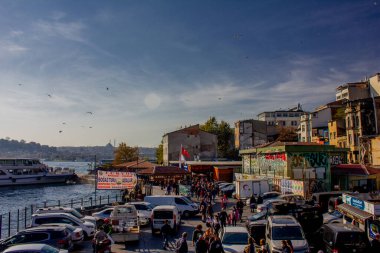 Eminonu, İstanbul, Türkiye-Ekim-Cumartesi-2021: Bulutlu hava, park edilmiş arabalar. Eski evlerin arasında yürüyen insanlar. Graffiti çizimi. Golden Horn Metro Köprüsü manzarası ve uçan martılar