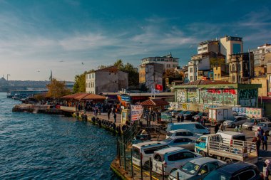 Eminonu, İstanbul, Türkiye-Ekim-Cumartesi-2021: Bulutlu hava, park edilmiş arabalar. Eski evlerin arasında yürüyen insanlar. Graffiti çizimi. Golden Horn Metro Köprüsü manzarası ve uçan martılar