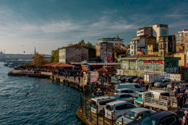 Eminonu, İstanbul, Türkiye-Ekim-Cumartesi-2021: Bulutlu hava, park edilmiş arabalar. Eski evlerin arasında yürüyen insanlar. Graffiti çizimi. Golden Horn Metro Köprüsü manzarası ve uçan martılar